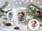 Preview: Weihnachtstasse mit niedlichem Bärchen in Weihnachtsmütze und Engelsflügeln, verziert mit dem Schriftzug 'Merry Christmas'. Perfektes Geschenk für die Weihnachtszeit, mit festlicher Dekoration im Hintergrund.